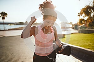 Smiling woman fist pumping while carry a yoga matt