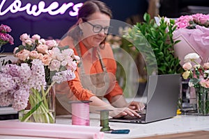 Smiling woman florist small business flower shop owner using laptop to take online orders