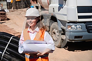 Smiling woman foreperson in safety vest and hardhat holding paper drafts