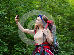 Smiling woman in the forest taking a selfie on a smartphone.