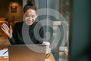 Smiling woman freelance talking with client via video call and discuss project sitting in cafe