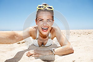 Smiling woman in funky glasses taking selfies at sandy beach