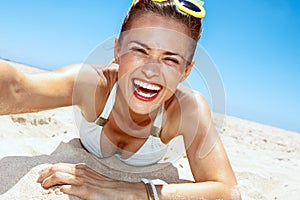 Smiling woman in funky glasses taking selfies at sandy beach