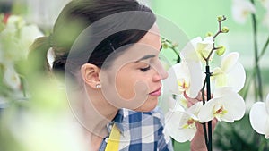 Smiling woman in garden of flowers, touches and smells an orchid