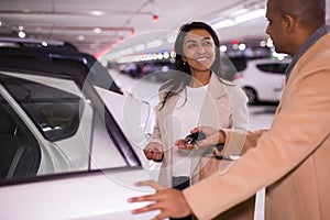 Smiling woman gets into a car in an underground parking lot. Man opens car door