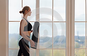 Smiling woman getting ready for meditation, holding yoga mat