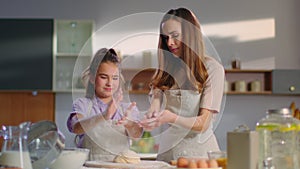 Smiling woman and girl shaking off flour on kitchen. Daughner helping mom.