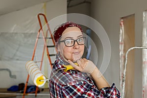 Smiling woman in glasses with a roller in hands is preparing for painting work