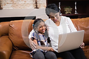 Smiling woman with granddaughter using laptop at home