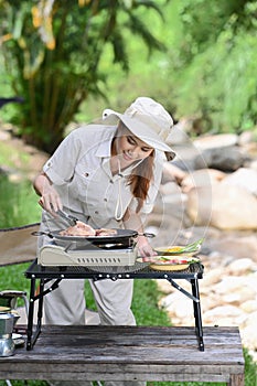 Smiling woman grilled bbq for dinner during camping on summer holiday. Travel, tour adventure on nature and vacation