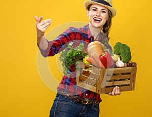 Smiling woman grower with box of fresh vegetables beckoning