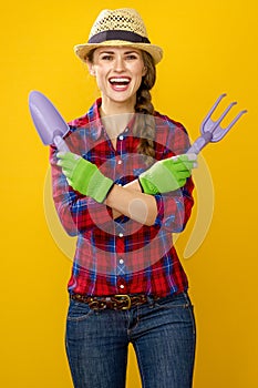 Smiling woman grower on yellow background with gardening tools