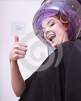 Smiling woman hair rollers curlers showing thumb up dryer beauty salon