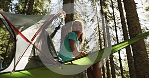 smiling woman in hanging tent camping in forest with sun flares sunlight.Group of friends summer adventure journey in