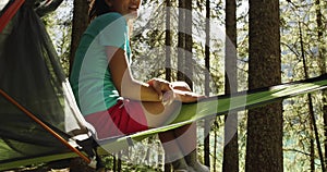 smiling woman in hanging tent camping in forest with sun flares sunlight.Group of friends summer adventure journey in