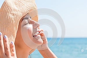 Smiling woman in hat is applying sunscreen on her face. Indian style