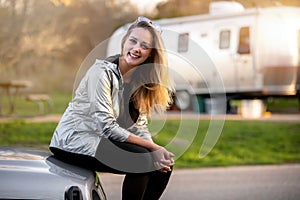 Smiling woman having fun camping outdoors with camper trailer RV, enjoying a fun experience outdoors