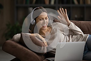 Smiling woman in headphones using laptop on couch, waving hand,