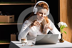 Smiling woman in headphones watching webinar on laptop in cafe