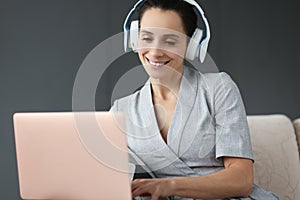 Smiling woman in headphones works behind laptop