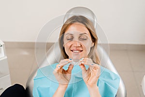 Smiling woman with healthy teeth holding removable clear braces aligner, orthodontic silicone trainer. Portrait girl