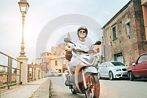 smiling woman in helmet and sunglasses fast riding the moto scooter on the Sicilian old town streets in the Forza d' photo