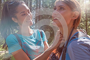 Smiling woman helping friend at hiking trail path in forest woods during sunny day.Group of friends people summer