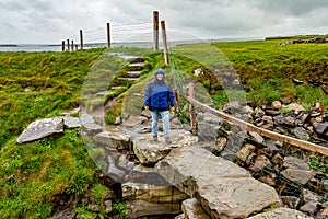 Smiling woman hiking on a stone bridge on the coastal walk route from Doolin to the Cliffs of Moher