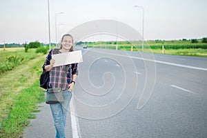 Smiling woman hitchhiker on the road is holding a blank board