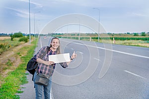 Smiling woman hitchhiker on the road is holding a blank board