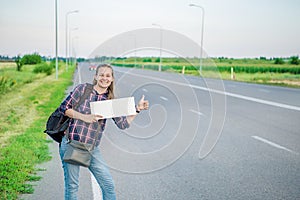 Smiling woman hitchhiker on the road is holding a blank board