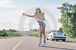 Smiling woman hitchhiker on road is holding a blank board.