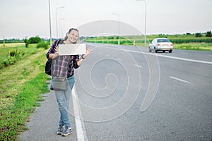 Smiling woman hitchhiker on the road is holding a blank board