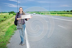 Smiling woman hitchhiker on the road is holding a blank board