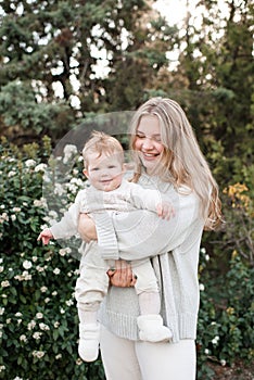 Smiling woman holding baby wearing trendy casual clothes over nature background outdoor.