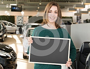 Smiling woman holding blackboard inside car dealership