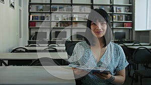 Smiling woman holding book in library. Friendly portrait with interactive atmosphere. Lifelong learning and community