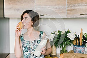 Smiling woman holding bread and milk bottle portrait on kitchen