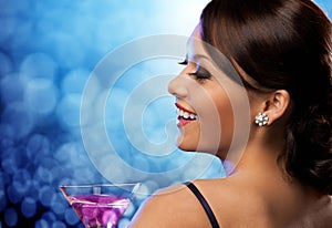 Smiling woman holding cocktail over blue lights