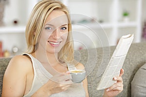 Smiling woman holding coffee and reading newspaper
