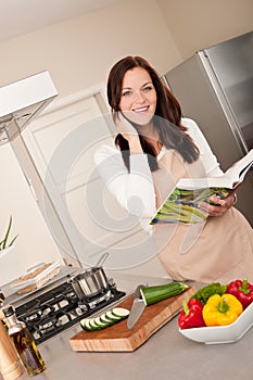 Smiling woman holding cookbook in the kitchen