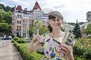 Smiling woman holding credit card and dollars shows thumb up