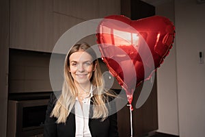 Smiling woman holding heart balloon in her hands, positive blonde girl with love symbol, valentine's day surprise