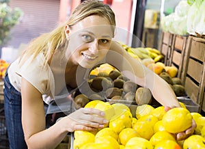 Smiling woman holding lemons in hands in fruit store