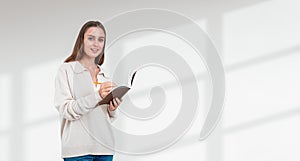 A smiling woman holding a notebook and a pencil on a white backg