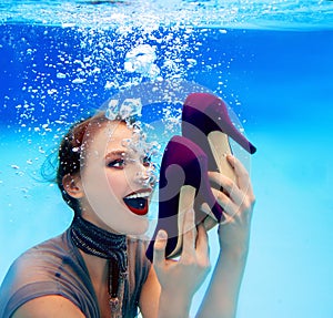 smiling woman holding a pair of shoes underwater in the swimming pool