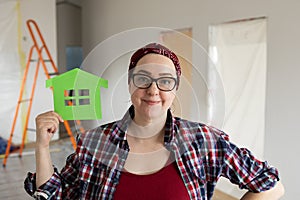 Smiling woman holding paper mockup of ecological green house near face