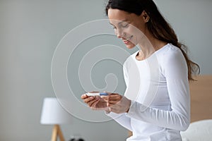 Smiling woman holding pregnancy test, waiting for result close up