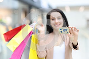 Smiling woman holding purchases and plastic bank card in shopping mall