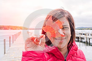 Smiling woman holding a red maple leaf in front of her face